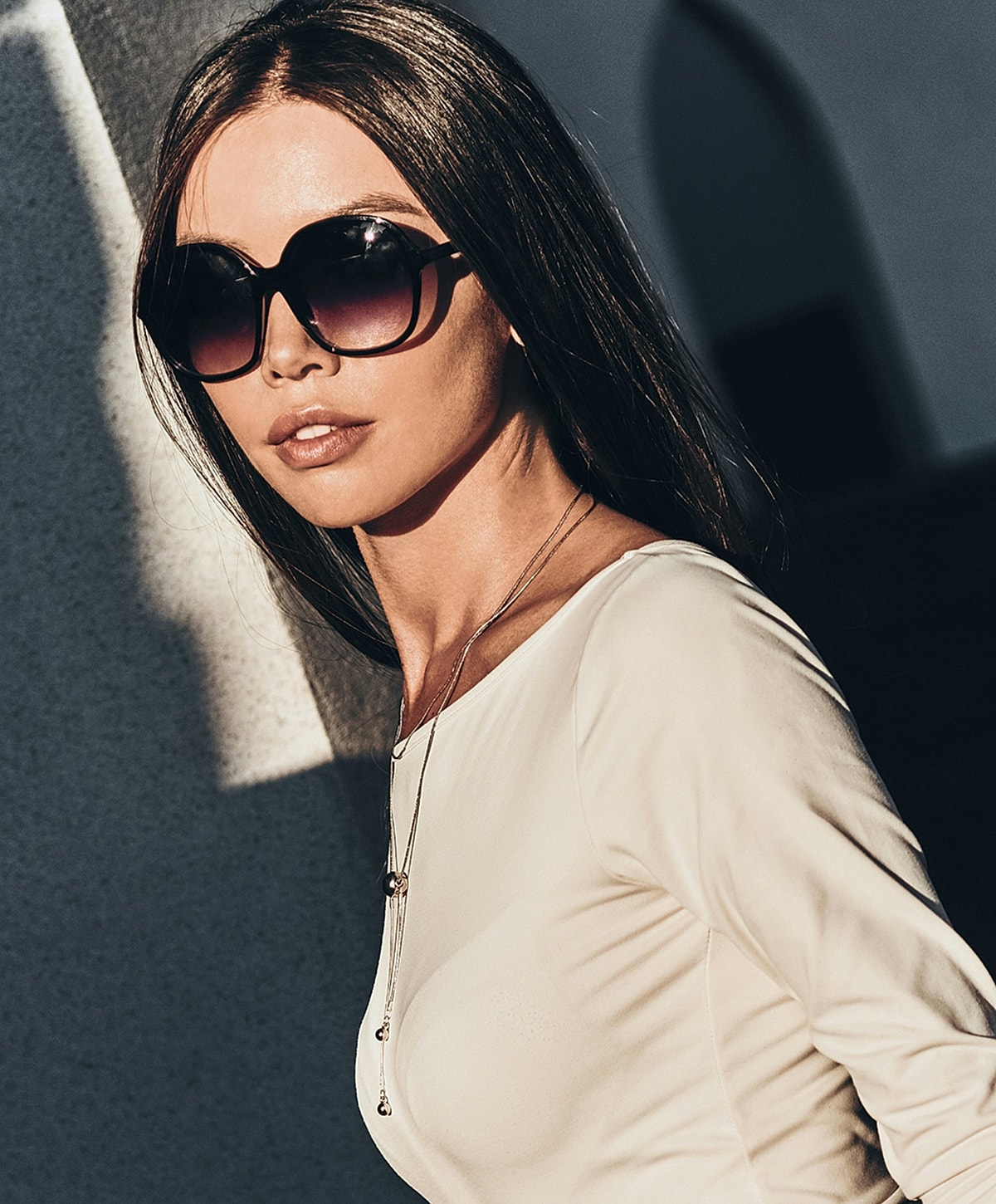 Woman in sunglasses with long hair and necklace.